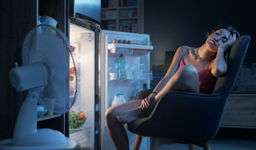 Woman sitting in front of open air conditioner with fan blowing at her due to broken AC.