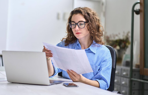 A man looking at documents while sitting in front of a laptop at a table.